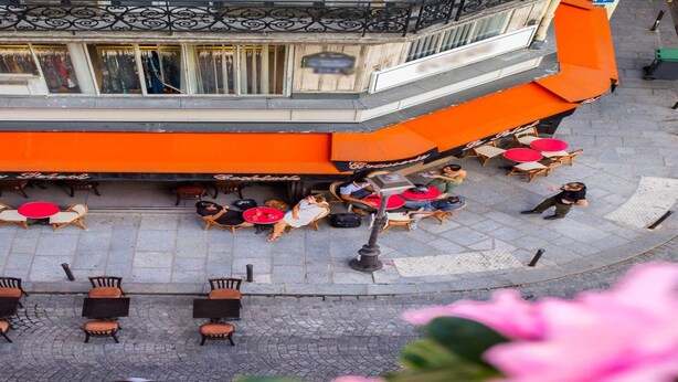 Ein Straçencafé mit orangefarbenen Markisen, Korbstühmeln und roten Tischen.
