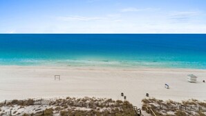 Une plage avec un ciel dégagé, un rivage sablonneux et quelques constructions, notamment un poste de surveillance pour les sauveteurs et un petit bâtiment.
