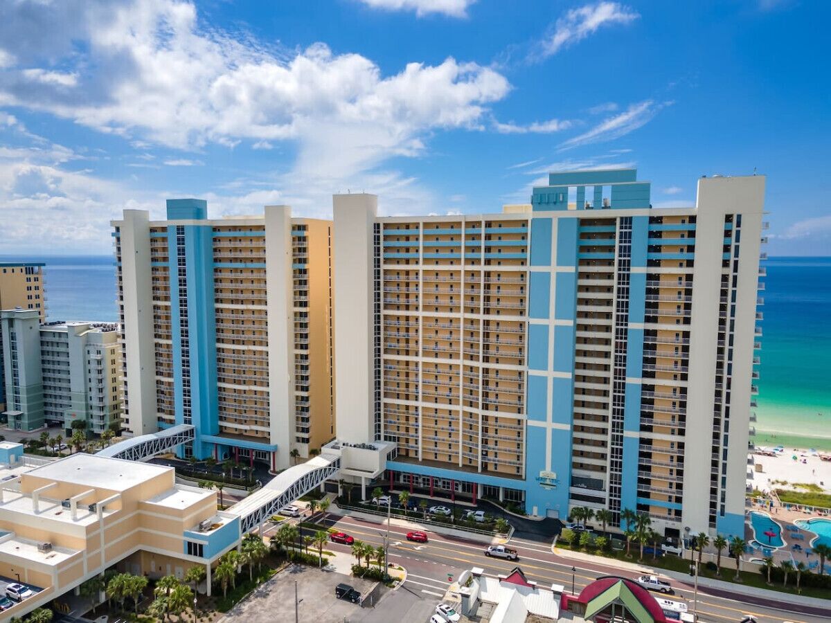 A high-rise hotel with multiple floors, a beach view, and a parking area in front.