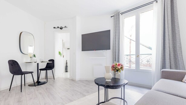 Een moderne woonkamer met een bank, een eettafel met stoelen, een flatscreen-televisie en een balkon met uitzicht.
