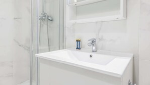 Een badkamer met een douchecabine van glas, een witte wastafel en een spiegel erboven.