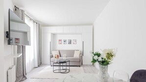 Een moderne, minimalistische woonkamer met een bank, een salontafel en een eethoek met een bloevas en wijnglazen.