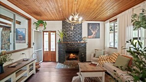 A cozy living room with a stone fireplace, wooden ceiling, and a large window. - Bellbird Rise Off-Grid Cottage (Conondale)