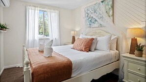 A neatly arranged bedroom with a bed, bedside tables, a window with curtains, a wall-mounted artwork, and a ceiling fan. - Bellbird Rise Off-Grid Cottage (Conondale)