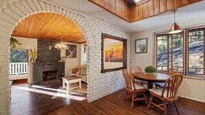 A dining area with a brick fireplace, wooden dining table, and chairs. - Bellbird Rise Off-Grid Cottage (Conondale)