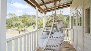 A porch with a hanging chair and a view of a forested area. - Bellbird Rise Off-Grid Cottage (Conondale)