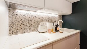 A kitchen with white cabinets, a speckled backsplash, a countertop with a toaster, a coffee maker, and a sink.