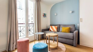 A modern living room with a grey sofa, two round wooden tables, a pink ottoman, and a blue ottoman.