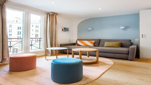 A modern living room with a grey sofa, two round wooden tables, a blue ottoman, and a pink ottoman.