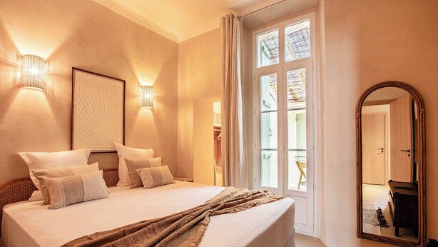 Hotelkamer met een groot bed, twee wandlampen, een grote spiegel en uitzicht door een raam.