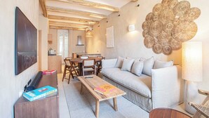 Een gezellige woonkamer met een bank, een houten salontafel en een televisie. Er is een eethoek met een tafel en stoelen, en een keuken op de achtergrond.