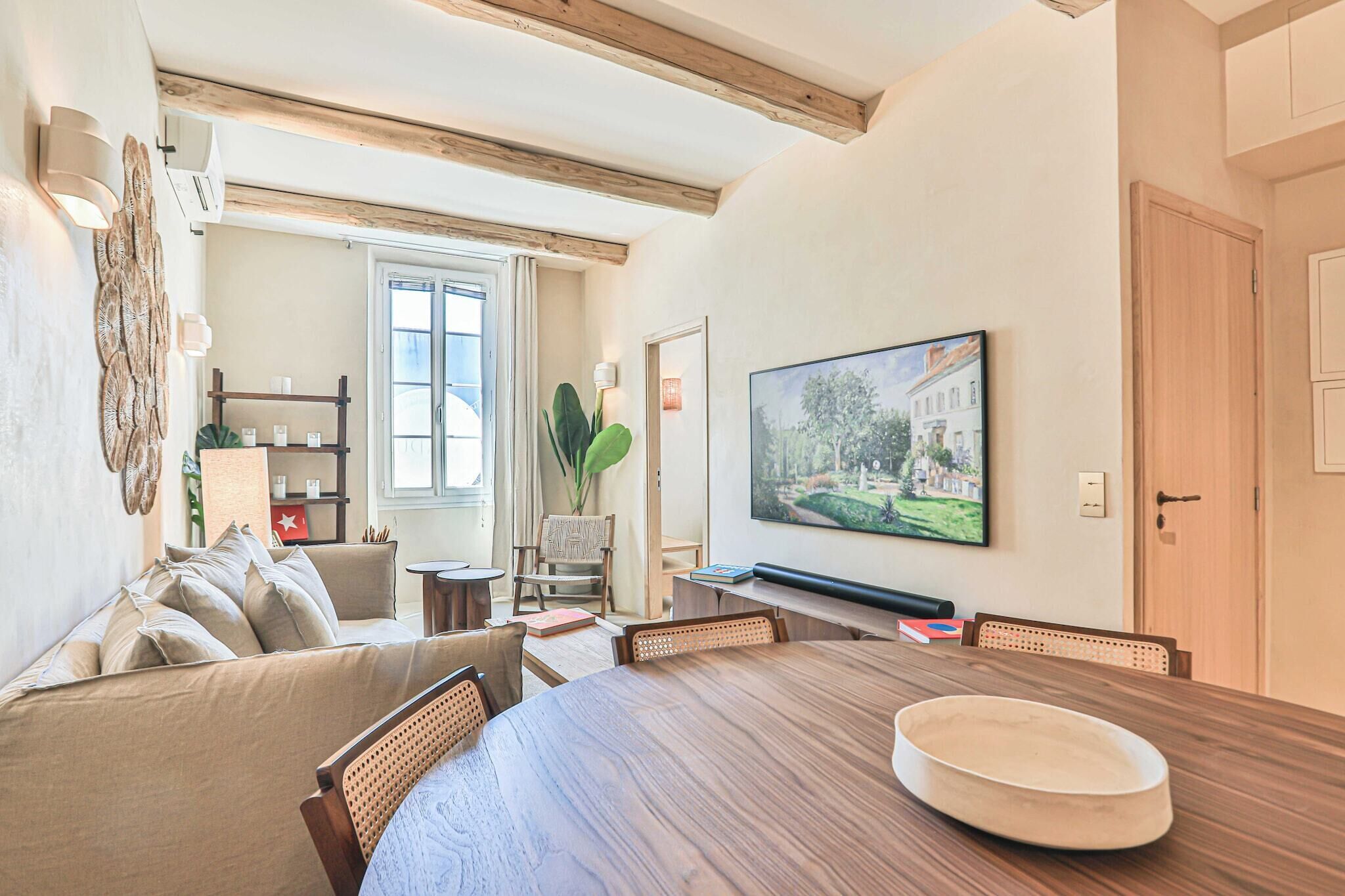 A dining area with a wooden table, chairs, a sofa, and a television mounted on the wall.