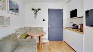 Ein stilvoller Wohnbereich mit einer Couch, einem runden Holztisch und einer Küchenzeile mit Fernseher und Schränken.