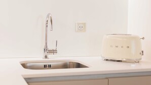 Una cucina con un lavandino in acciaio inox, un tostapane bianco e una presa a muro.