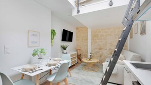 Ein gemütlicher Wohnraum mit Essbereich, einer Couch, einem kleinen runden Tisch und einem an der Wand befestigten Fernseher.