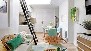 Ein modernes Wohnzimmer mit einer Couch, einem Esstisch mit Stühlen, einer Treppe und einem an der Wand befestigten Fernseher.