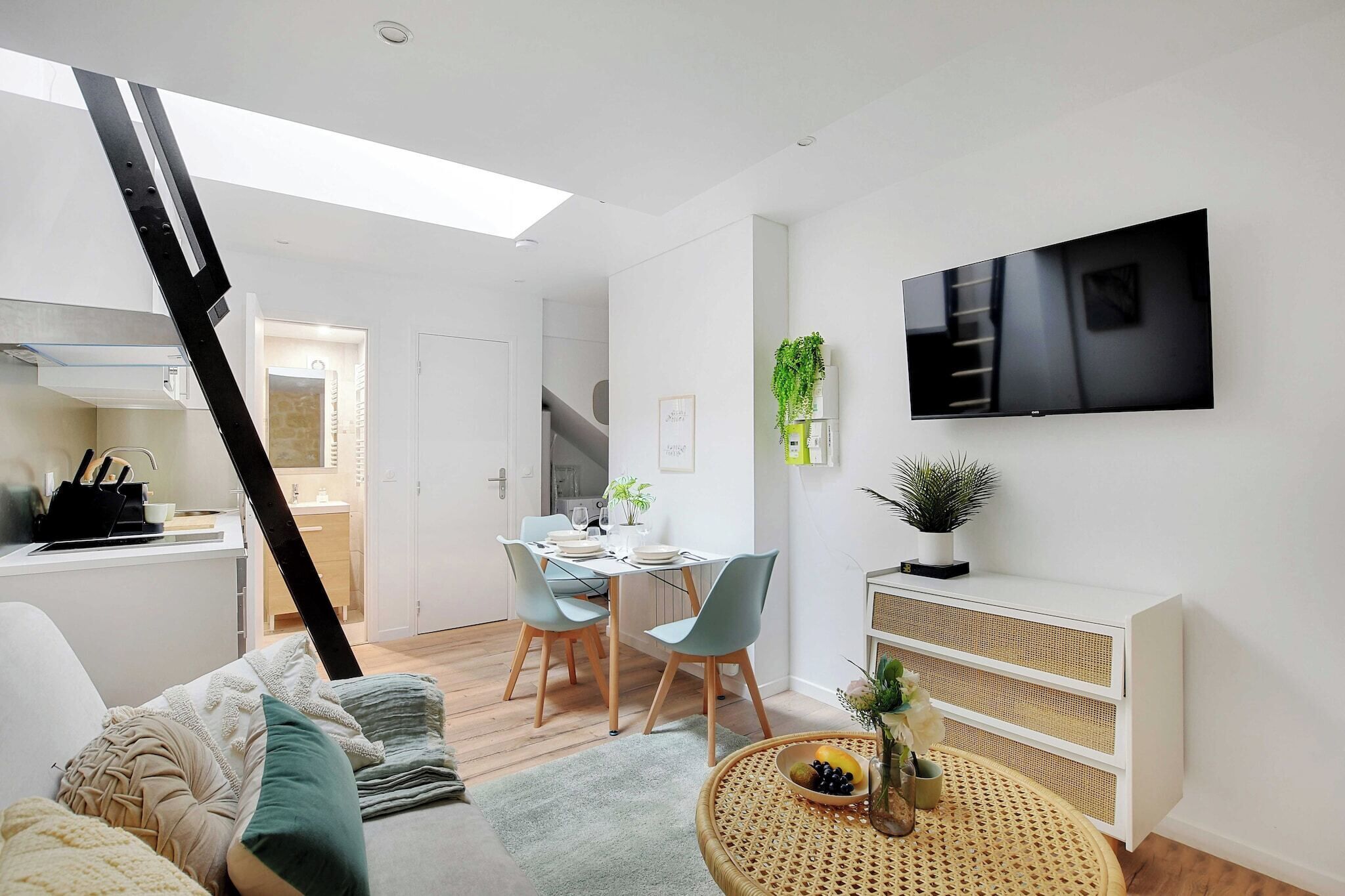 Un espace de vie moderne comprenant un coin repas, un canapé, un téléviseur fixé au mur et un escalier menant à une autre pièce.