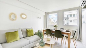A modern living room with a grey sofa, green cushions, a dining table set for four, and two round mirrors on the wall.
