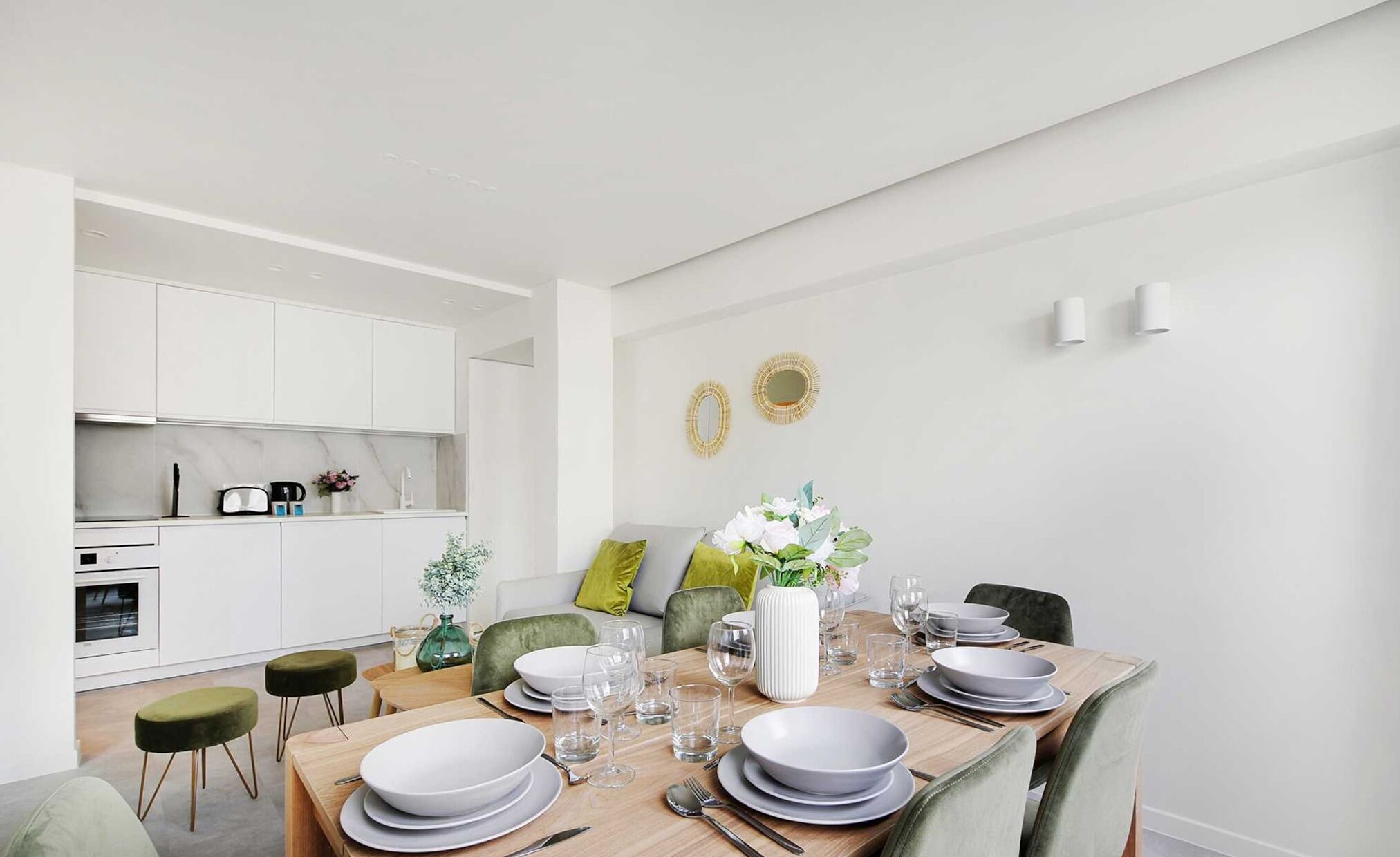 A modern dining area with a wooden table set for four, white plates, and clear glasses.