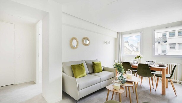 A modern living room with a sofa, dining table, chairs, and a window with a view of buildings.