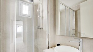 A modern bathroom with a glass shower enclosure, a white sink, and a large mirror.