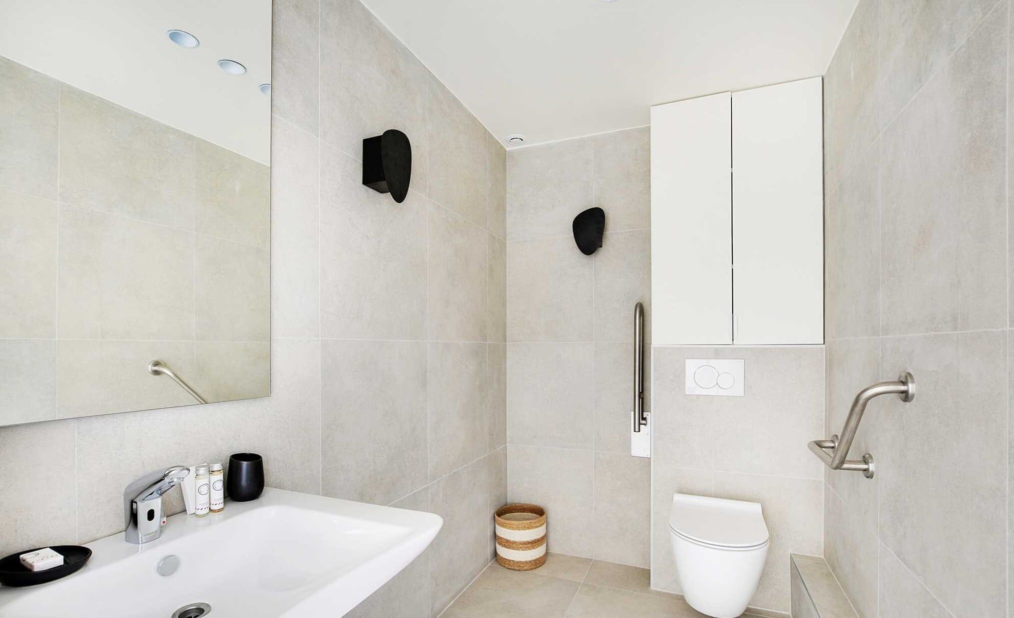 A modern bathroom with a white sink, a mirror, a toilet, and a shower area.