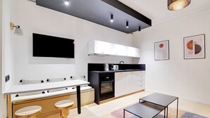 Una cucina moderna con un piano di lavoro bianco, mobili neri e forno integrato. Sono presenti due sgabelli di legno e un tavolino.