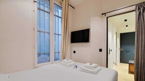 Una camera d'albergo con un letto, una TV a muro e una porta che dà su un balcone.