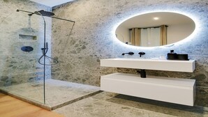 A modern bathroom with a stone wall, a glass-enclosed shower, a white vanity with a mirror, and a built-in heater.