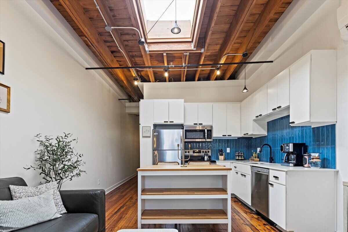 A modern kitchen with white cabinets, a wooden ceiling, and a skylight.
