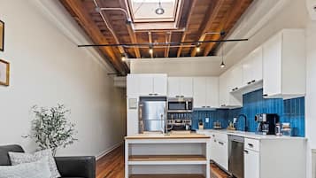A modern kitchen with white cabinets, a wooden ceiling, and a skylight.