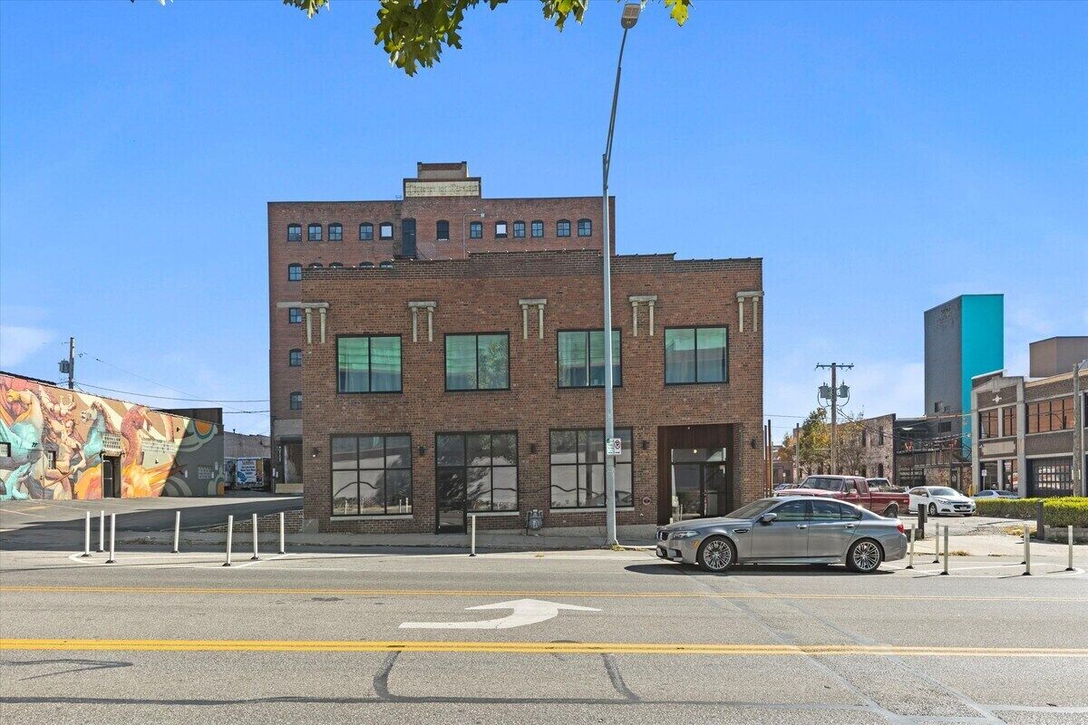 A multi-story building with a brick facade, large windows, and a parking lot with cars.