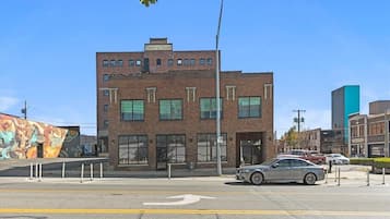 A multi-story building with a brick facade, large windows, and a parking lot with cars.