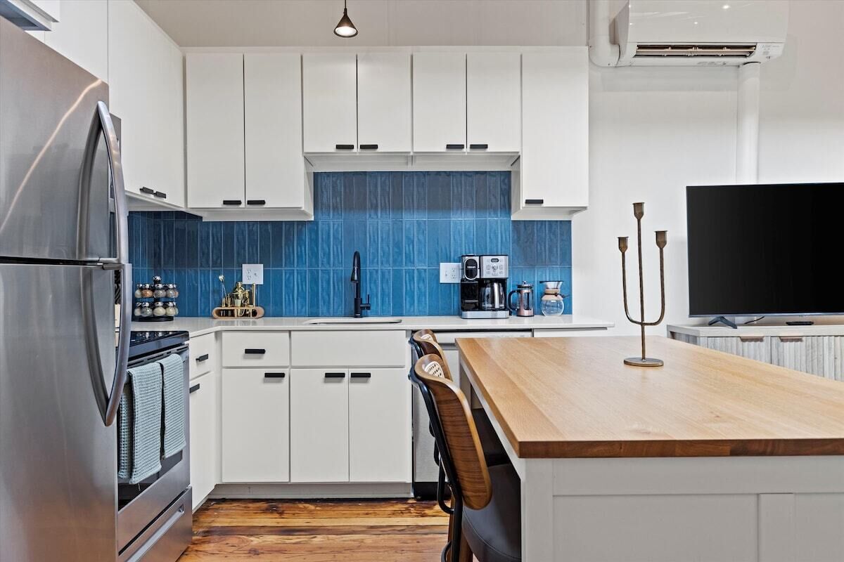 Een moderne keuken met witte kasten, een blauwe achterwand, een houten eiland en een flatscreen televisie.