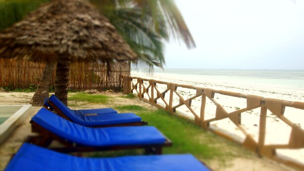 A beachside lounge area with blue lounge chairs and a thatched-roof structure. - AMANI BEACH VILLA (Bwejuu)