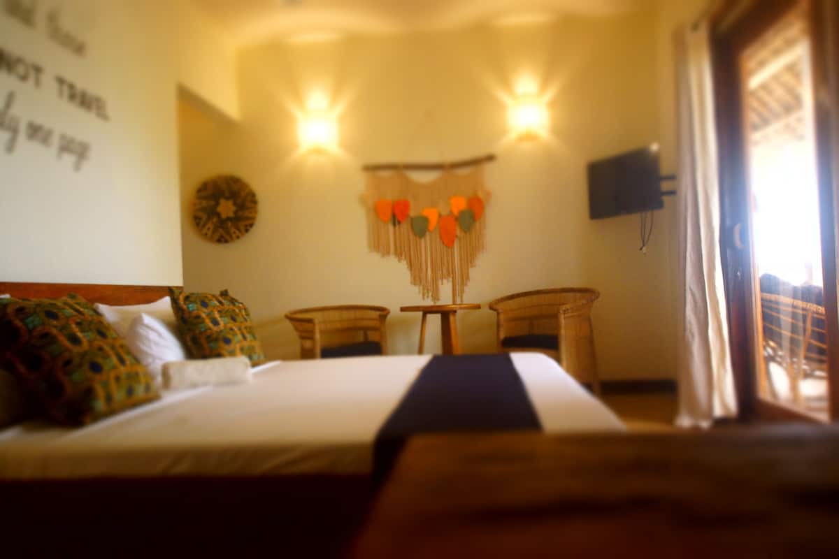 Habitación de hotel con una cama, dos sillas, un televisor montado en la pared y un adorno decorativo en la pared.
