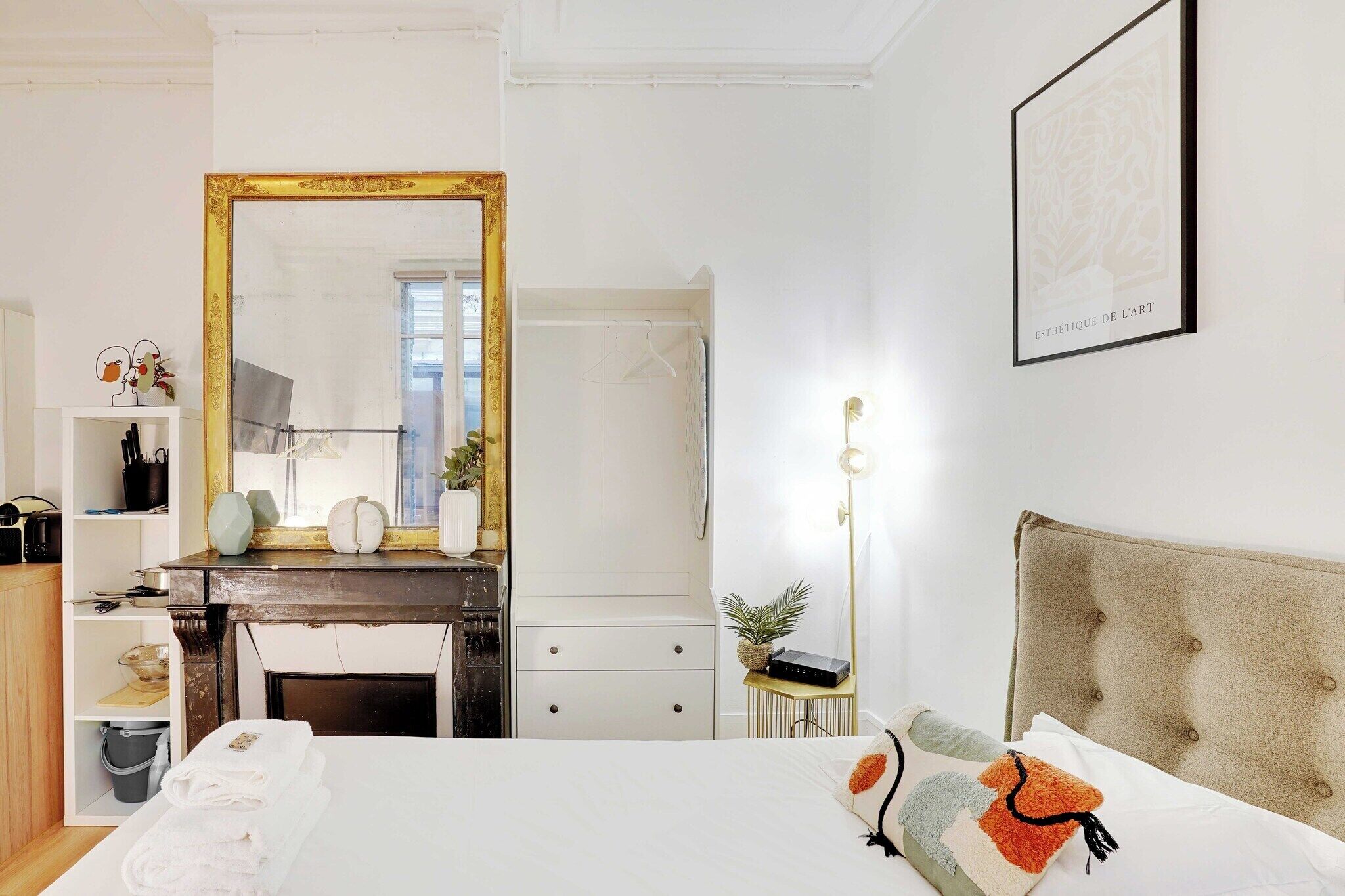 A hotel room with a large mirror, a bed with decorative pillows, a dresser, and a bedside table with a lamp.
