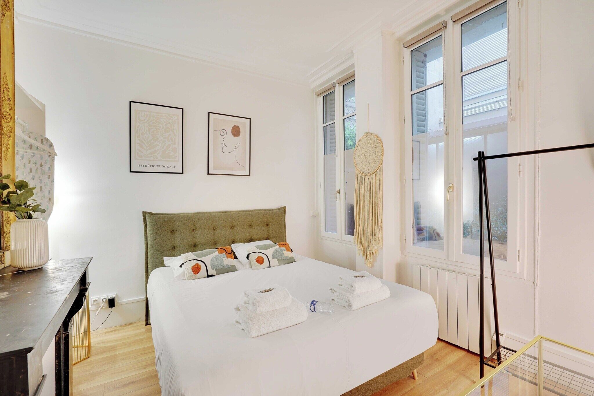 Une chambre à coucher bien aménagée, avec un lit, une table de chevet, une fenêtre donnant sur un beau paysage et des œuvres d’art accrochées au mur.