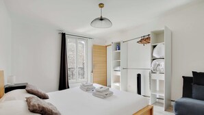 Quarto moderno com cama, guarda-roupa, área de estar e janela.