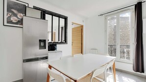 Cozinha compacta com geladeira, cafeteira e área de refeições com mesa e cadeiras.