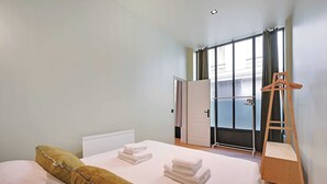 A bedroom with a bed, towels, a wooden ladder, and a view of the outside through a window. - Haven of peace near the Palais de Garnier (Paris)