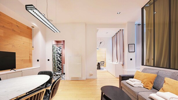 A modern living room with a dining area, a sofa with cushions, a TV, and a large window with curtains. - Haven of peace near the Palais de Garnier (Paris)