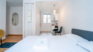 A hotel room with a bed, a desk, a chair, a mirror, and a kitchenette. - Charming studio- 2P- Jardin des plantes/Austerlitz (Paris)
