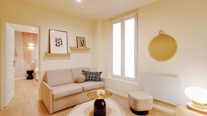 Un salon moderne avec un canapé, une table basse, un pouf et des œuvres d’art accrochées au mur.