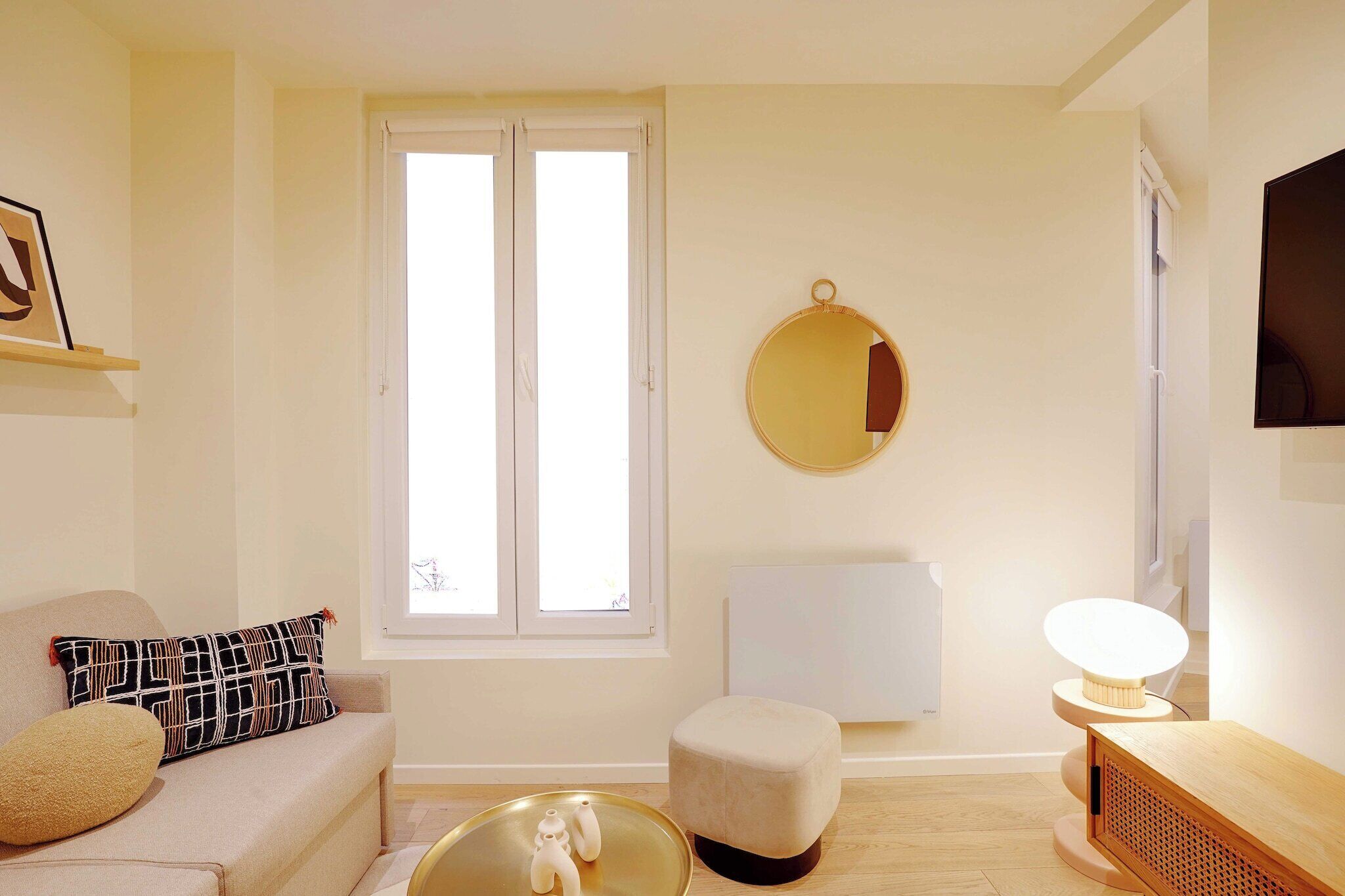 A modern living room with a sofa, ottoman, and a round mirror on the wall.