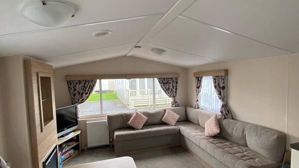 A compact RV interior with a sofa, a small table, a TV, and a window with curtains. - 2 bed Caravan in Rhyl , dog Friendly, With Wifi (Rhyl)