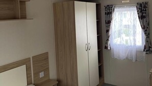 A bedroom with a bed, a wardrobe, a window with curtains, and a ceiling light. - 2 bed Caravan in Rhyl , dog Friendly, With Wifi (Rhyl)