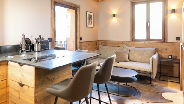 Eine gemütliche Küche mit einer Holztischinsel, Barhocker und einer Couch. Es gibt ein Fenster mit Blick, ein Bild an der Wand und eine Leuchte über der Arbeitsfläche.