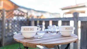 Zwei weiße Tassen mit 'PETIT DEJ.' darauf, ein Löffel und klare Gläser auf einem Holztisch.