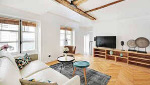 A modern living room with a high ceiling, wooden beams, a sofa, a TV, and a decorative shelf.